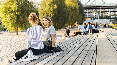 Zwei Frauen sitzen im Park am Gleisdreieck auf einer Sonnentribüne und unterhalten sich
